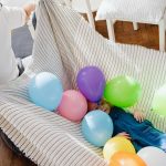 A joyful moment inside with a father and daughter playing with colorful balloons.